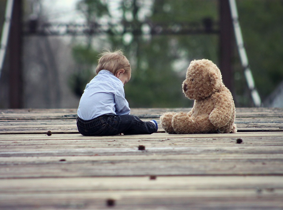 a boy and his teddy bear sit on the wooden deck seem lonely