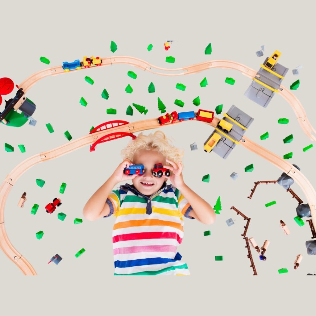 child lies and smiles in the middle of wooden rail track with trains on the path 