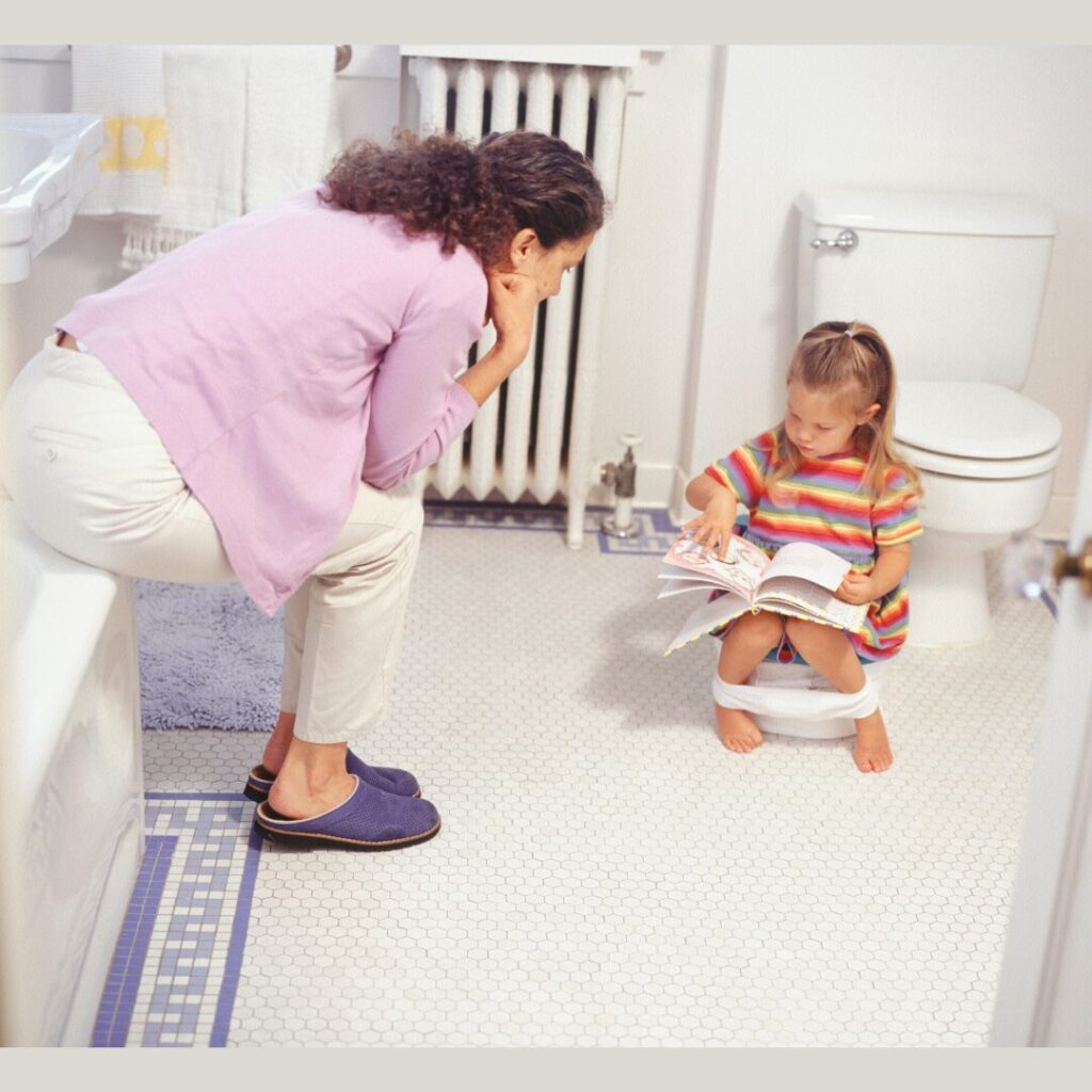 child sits on a potty and mom is sitting near to her full of support and engagement